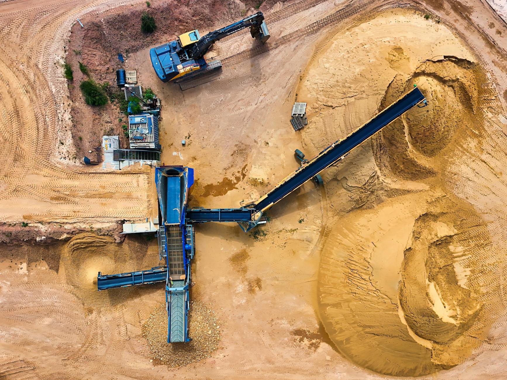 A bulk carrier is loaded at an iron ore export terminal as industrial workers operate near port infrastructure.